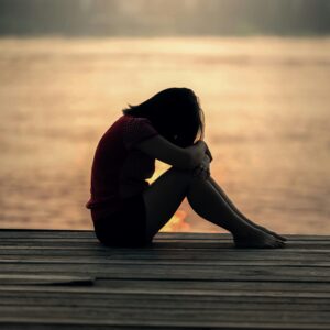 A sad woman sitting on the boardwalk beside a beach