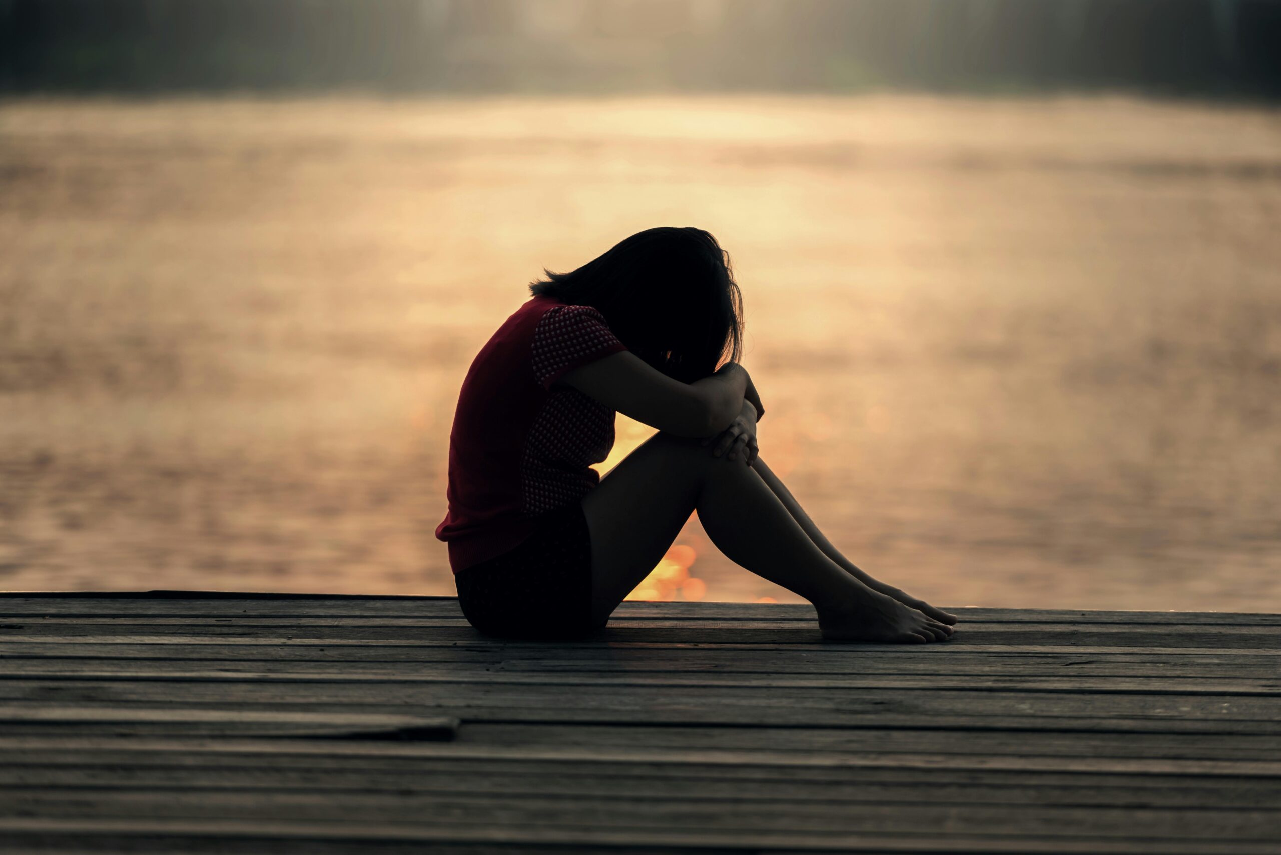 A sad woman sitting on the boardwalk beside a beach